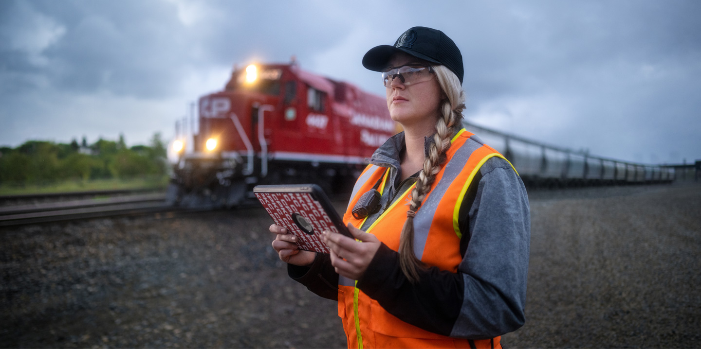 Une cheminote tenant un iPad regarde la voie ferrée au passage d’un train
