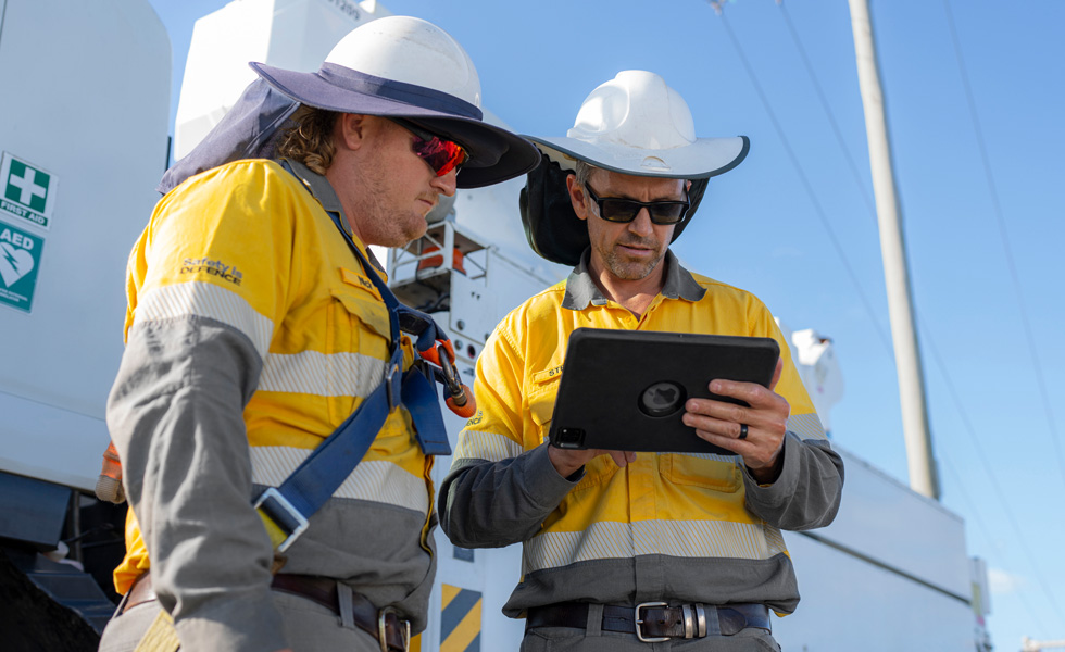 Deux hommes de terrain collaborent sur un iPad, debout à côté d’un camion de service