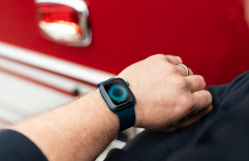 Près d’un camion d’incendie, une Apple Watch au poignet d’une personne affiche un message indiquant qu’il est temps de prendre une bonne inspiration.