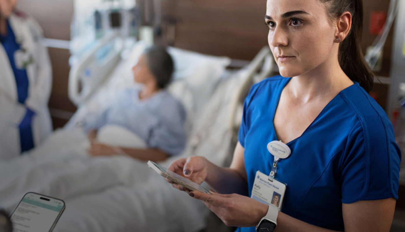 Une infirmière saisit du texte sur son iPhone tandis qu’une autre soignante parle avec une personne hospitalisée.