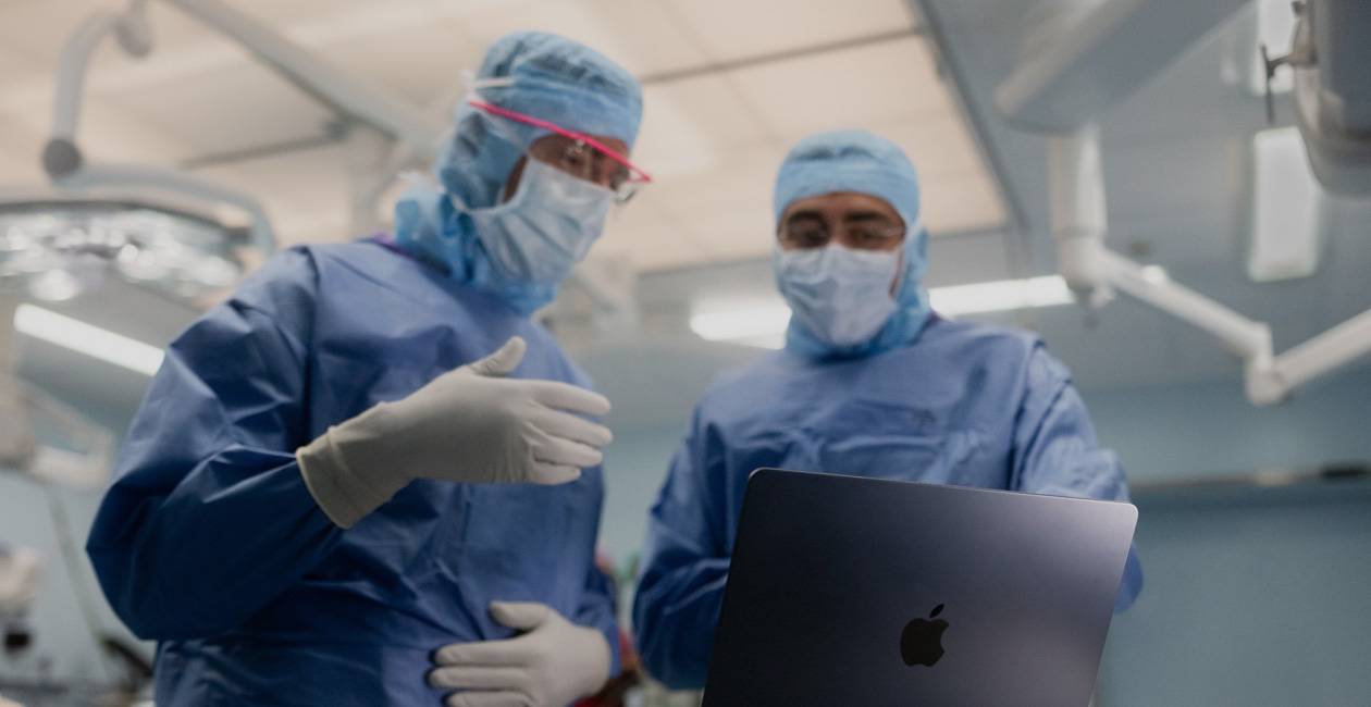 Deux chirurgiens en discussion devant un écran de MacBook Pro au bloc opératoire.